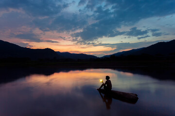 Beautiful landscape Silhouette image with mountains reflecting the blue sky of the river. The clouds and the orange light in the sunset and the shadow of a man with a mobile flash.