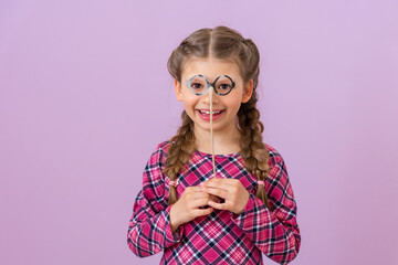 A little girl holds a pair of fancy dress glasses near her face.