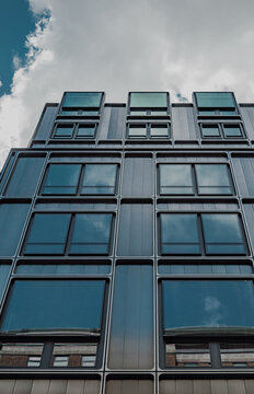 Vistas de un edificio con ventanas de marco redondeado desde abajo. Arquitectura contempor&aacute;nea, con grandes ventanales de cristal que muestran el reflejo del cielo en tonos azulados y turquesa