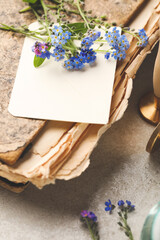 Beautiful Forget-me-not flowers and antique book on grey table, closeup