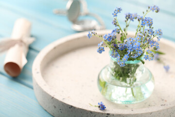 Beautiful  Forget-me-not flowers in vase on light blue wooden table. Space for text
