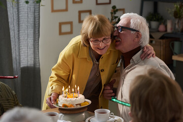 Happy senior couple embracing at the table while celebrating their anniversary with cake at home