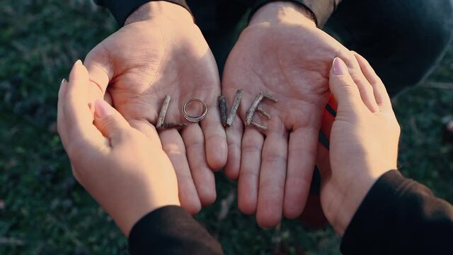 Close-up top view with the hands of two lovers holding the word love in their palms. Couple in love in nature. Marriage proposal