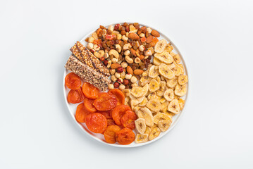 Granola bar, dried apricots, dried bananas, nuts and dried fruits in a white flat plate on a light background.
