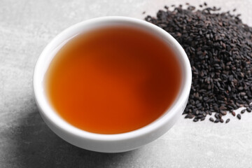 Fresh oil in bowl and black sesame seeds on grey table, closeup