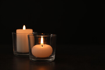 Burning candles in glass holders on table against dark background, space for text