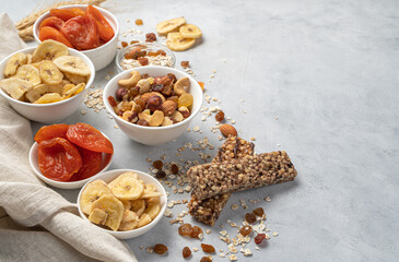 Assortment of nuts, dried fruits and granola bar on a gray background.