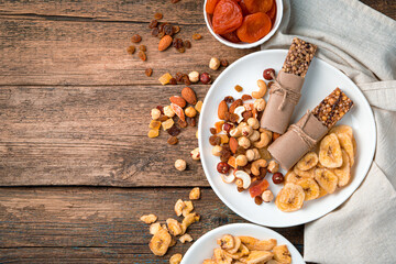 Natural, healthy sweets. Granola bar, nuts, dried fruits in a white plate on a wooden brown background.