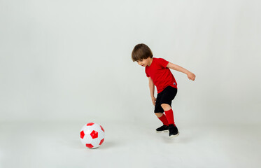 small boy in uniform plays with a soccer ball on a white background with space for text