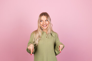 Pretty european woman in casual knitted sweater on pink background happy amazed excited point down with index finger copy space