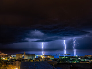 Closeup of lightnings striking on the ocean from the gloomy skies at night framed  coastal buildings