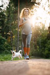 Young happy woman doing weight loss fitness in the park, running with her dog jack russell.