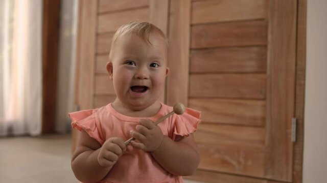 Happy baby girl down syndrome play have fun with her family at home. hild hits a xylophone with a stick.