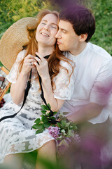 Enamored man hugs his girlfriend while sitting on green grass in the park. Happy couple at picnic