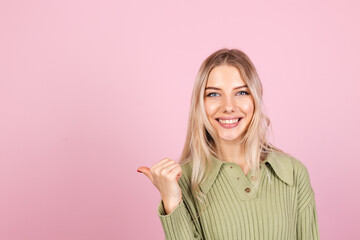 Pretty european woman in casual sweater on pink background happy smiling point left with thumb finger