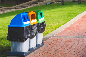 Perspective side view of 3 colorful garbage bins for separate waste sorting on stone tiles pavement in public park area