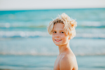 Portrait of cute teen boy with blond hair posing against the sea.