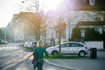 Fototapeta na wymiar Rear view of beautiful elegant carefree woman walking on the street with sunlight flare