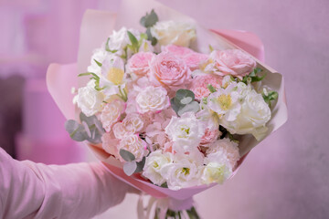 A hand holds a lush bouquet of light pink, white cute delicate small roses of different sizes, flowers of green leaves. Paper packaging. Romance.
