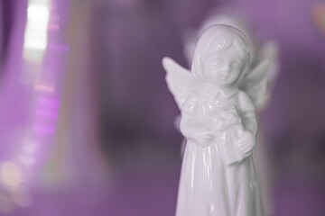 Small white marble figurine of an angel in dress on a light pink blurred bokeh background. Close-up. Place for text