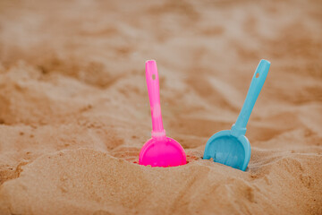 Fototapeta na wymiar Pink and blue plastic toy spades forgotten on the sand sea coast.