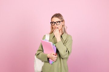 Pretty european woman in casual sweater on pink background with notebooks nervous worried gnawing nails education concept