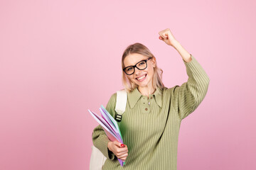 Pretty european woman in casual sweater on pink background with notebooks clenching fist winner gesture gesture education concept