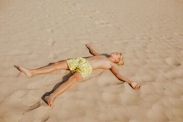 Boy laying on sand beach and playing the angel. Summer time concept. Copy space.