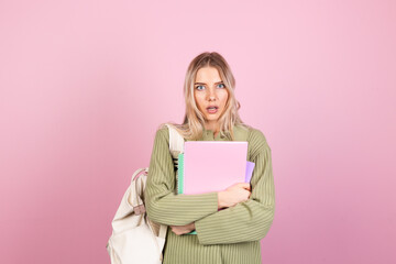 Fototapeta na wymiar Pretty european woman in casual sweater on pink background with notebooks shocked look to camera with open mouth, education high school concept