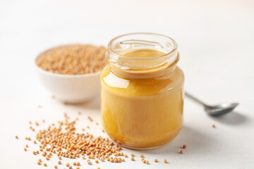 Mustard sauce in jar and seeds on a bright background.