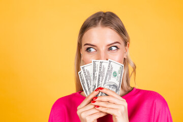 Pretty european woman in pink  blouse on yellow background hold fan of 100 dollars money and, excited surprised cover face