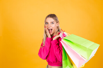 Fototapeta na wymiar Pretty european woman in pink blouse on yellow background holding shopping bags shocked amazed excited isolated copy space
