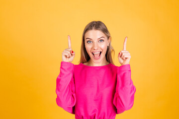 Pretty european woman in pink  blouse on yellow background happy excited cheerful point up with index finger