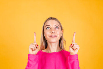 Pretty european woman in pink  blouse on yellow background happy excited cheerful point up with index finger