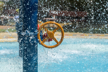 Children's water park spray splash pad looking to turning wheel in the sunshine and water spray. © KingmaPhotos