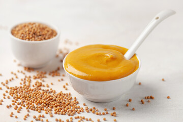 Mustard sauce in a bowl and seeds on a bright background.