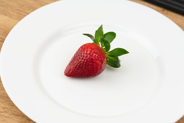 Red ripe strawberry berry on white plate on the table close up