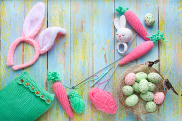 pascahl composition of knitted rattle and carrots and a nest with small birds and eggs on a textured wooden background