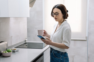 woman drinking coffee in the kitchen while using her smartphone
