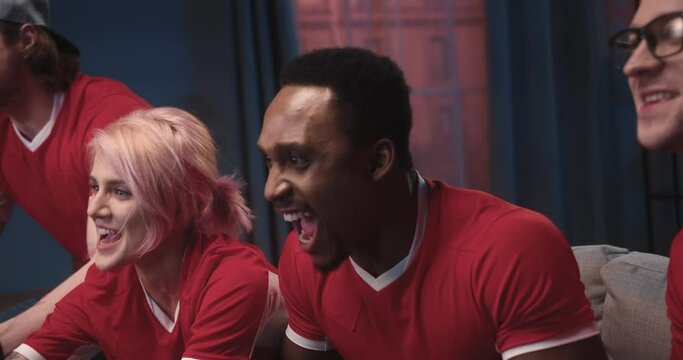 Close up of happy young cheerful multi-ethnic men and women at home on couch feeling excited cheering for fav team and it winning championship game. Friends watch sport event on TV, fun concept