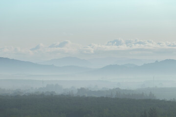 The trees are foggy in the morning with a mountain background and white clouds. Is a view from a height