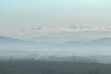 The trees are foggy in the morning with a mountain background and white clouds. Is a view from a height