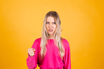 Pretty european woman in pink blouse on yellow background shouts angrily, reproachfully accuses you, points directly to camera, blames you