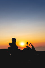 Fototapeta na wymiar Woman biker silhouette over sunset, female riding motorcycle, motorbike driver traveling, lady look on the beach, freedom lifestyle. travel and vacation. Vertical photo