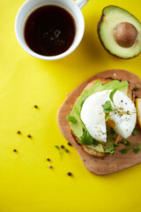 Cup of black coffee and sandwich with avocado and poached egg, seeds and microgreen. Yellow background. Copy space. Healthy breackfast