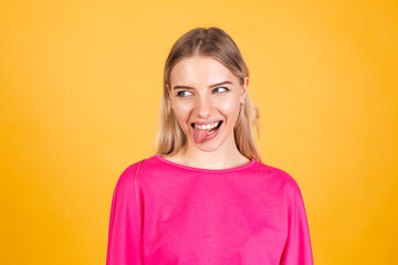 Pretty european woman in pink blouse on yellow background sticking tongue out happy with funny expression does funny grimaces
