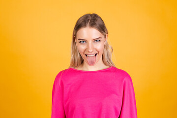 Obraz premium Pretty european woman in pink blouse on yellow background sticking tongue out happy with funny expression does funny grimaces