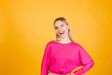 Pretty european woman in pink blouse on yellow background sticking tongue out happy with funny expression does funny grimaces