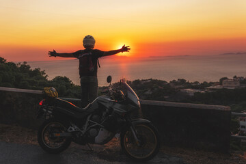 Fototapeta na wymiar Motorcyclist man enjoy beautiful sunset arms spread out to the sides, sea and mountains. Destination. Motorcycle tour journey. copyspace for your individual text.