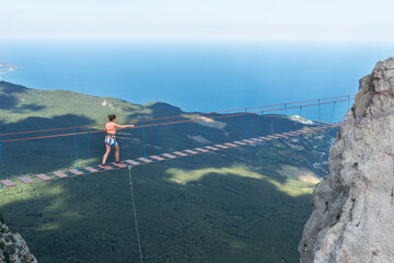 Young girl cross  long aerial rope bridge on peak of Ai-Petri mountain in Crimea. Girl is brave and courage during adventure in mountains, Active lifestyle.